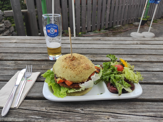 Ein Teller mit einem Burger darauf und einem Salat zur Seite. Ein Glas Bier dahinter.