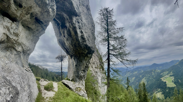 Offenes Felsentor in einer Felswand mit Bergpanorama Blick 