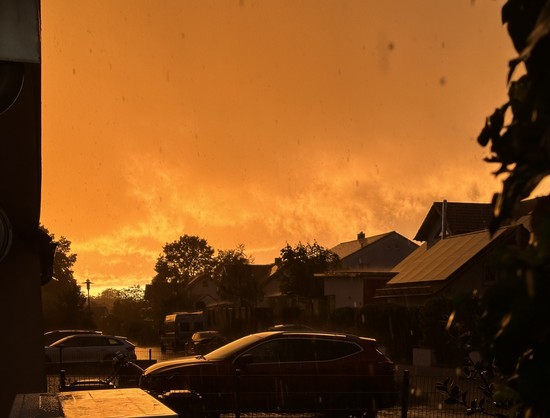 Blick auf eine Häuserzeile mit Sonnenuntergang im Hintergrund und Regenschauer. In tief orange getauchte Farbenpracht.