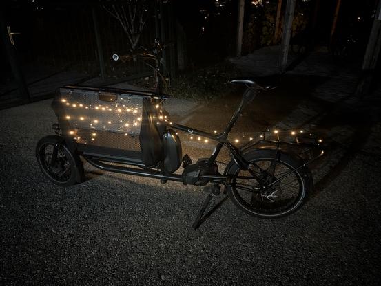 Black cargo bike at night with LEDs mounted on its left hand side.