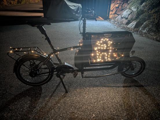 Black cargo bike at night with LEDs mounted on its right hand side, resembling a reindeer.