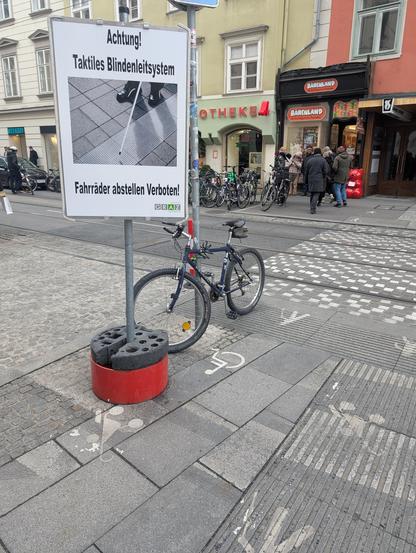 Temporäres Schild in der Innenstadt in der Nähe eines Fußgängerübergangs:

Achtung!
Taktiles Blindenleitsystem
(Bild von einem Blindenstock, der Leitrillen folgt)
Fahrräder abstellen Verboten! (sic)
Holding Graz Stadtraum
