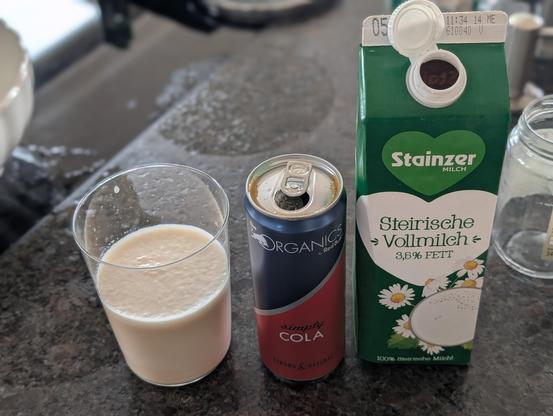 Glas mit Milch-Cola-Gemisch auf einer Küchenplatte stehend neben Red Bull Organics Cola und Stainzer Vollmilch