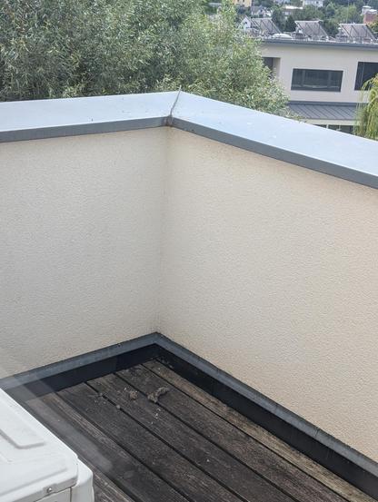 Reste eines Wespennests, das im Eck innen unter der Metallabdeckung gebaut wurde liegen am Holzboden verstreut. Irritierte Wespen fliegen um das alte Nest als auch über den Bruchstücken. Brösel liegen noch oben am Metall und zeugen vom Zerlegen des Bauwerks.