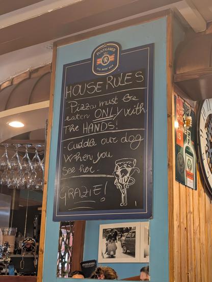 Blackboard in an old-fashioned restaurant which reads:

HOUSE RULES

Pizza must be eaten ONLY with the HANDS!

Cuddle our dog when you see her

GRAZIE!