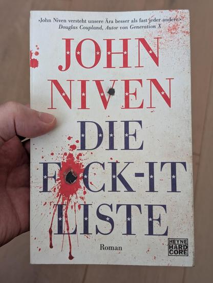 Cover des Taschenbuchs von "Die Fuck-It Liste" in einer Hand gehalten