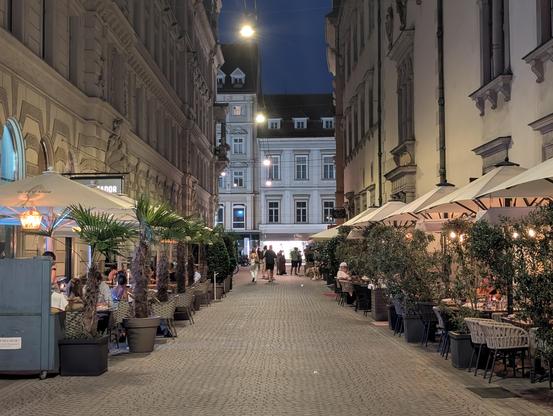 View into Landhausgasse at dawn with people sitting beneath the street, having fun, drinking and eating.