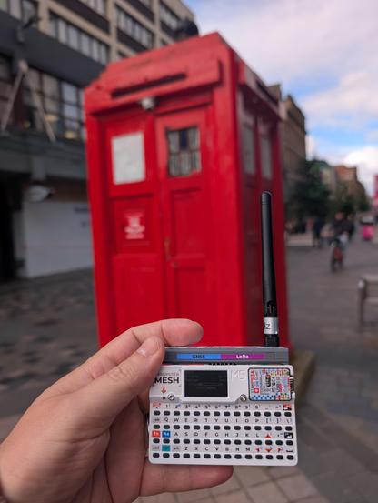 old English police phone box in background and a modern S3 Cardputer with Mesh addon in foreground running Meshtastic ROM
