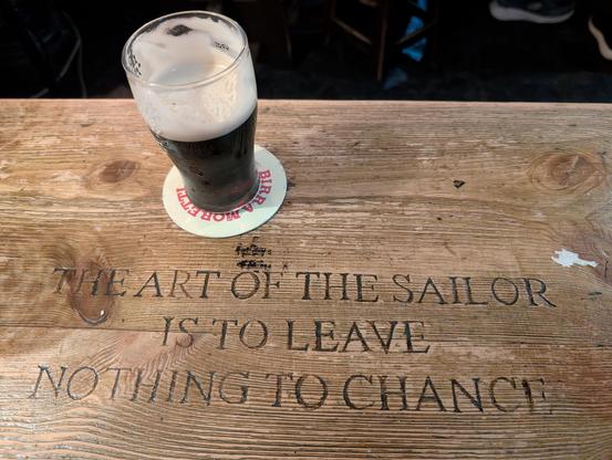 half a pint of Guinness on a wooden table which has carved in:

The art of the sailor
is to leave
nothing to chance